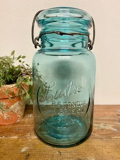 a blue mason jar sitting on top of a wooden table next to a potted plant