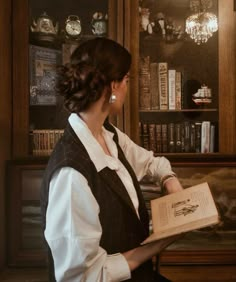 a woman holding an open book in front of a bookshelf filled with books