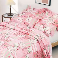 a bed covered in pink and green quilts next to a night stand with a lamp