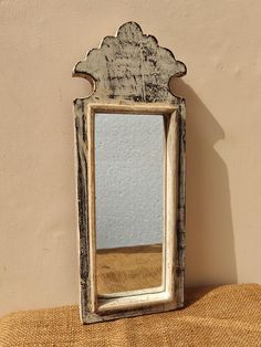 an old mirror sitting on top of a table next to a wall with a plant growing out of it