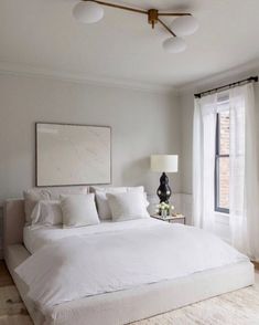 a large white bed sitting in a bedroom next to two lamps and a painting on the wall