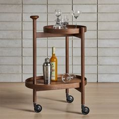 a wooden bar cart with two wine glasses and bottles on the top, sitting in front of a brick wall