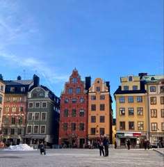 some people are standing in the middle of a square with buildings on both sides and blue sky above