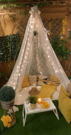 a white tent sitting on top of a lush green field next to a table with yellow pillows