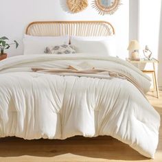 a bed with white comforter and pillows in a bedroom next to a plant on the floor