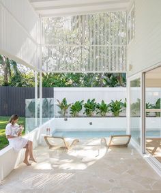 a woman sitting on a wall next to a swimming pool in a house with white walls