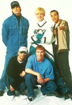 four young men posing for a photo in front of a white background with one man wearing a blue shirt