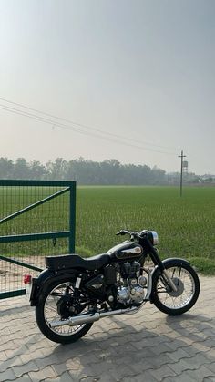 a black motorcycle parked in front of a green gate on a cobblestone road