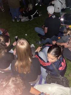 a group of people sitting on the ground looking at their cell phones and taking pictures