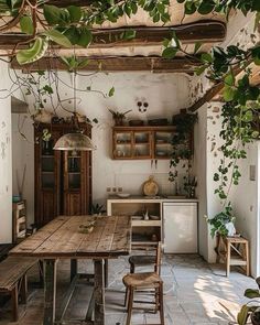 an old fashioned kitchen with wooden table and stools in the center, surrounded by greenery