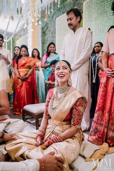 a woman sitting on the ground in front of other people at a wedding ceremony and laughing