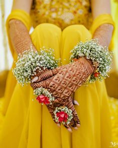 a woman in yellow dress holding her hands with flowers on the wrist and hendi