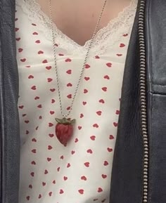 a woman wearing a white shirt and black leather jacket with a red strawberry pendant on it