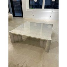 a white marble coffee table sitting on top of a floor next to two large windows