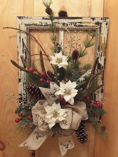 a christmas wreath with white flowers and pine cones hanging on a wooden door hanger