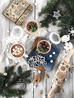 a wooden table topped with bowls filled with desserts and marshmallows next to christmas decorations