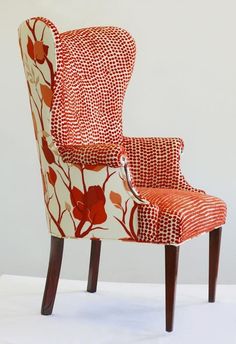 an upholstered chair with red and white floral fabric on the back, sitting in front of a wall