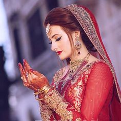 a woman dressed in red and gold holding her hands together while looking down at the ground