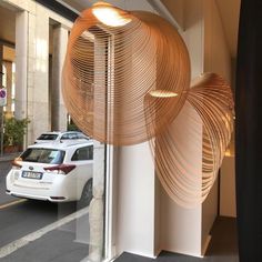 a white car is parked in front of a building with large wooden circles hanging from it's windows