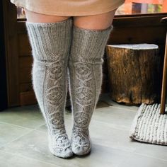 the legs of a woman wearing knee high socks and knitted stockings, standing in front of a window