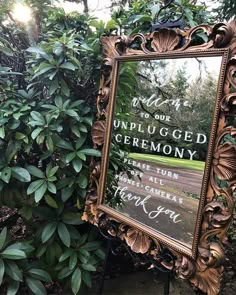 there is a mirror that has been placed in front of some bushes and trees with writing on it