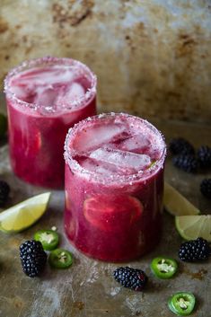 two glasses filled with blackberry margaritas next to lime slices and blackberries on a table