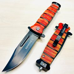 two knives are laying next to each other on a white surface with orange and black straps