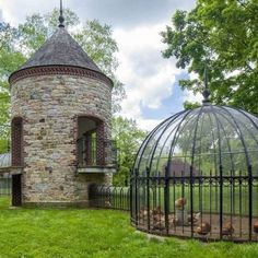 an old brick building with a cage in the front and chickens inside it on the lawn