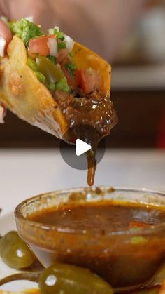 a person is dipping some food into a bowl with chili and green peppers on the side