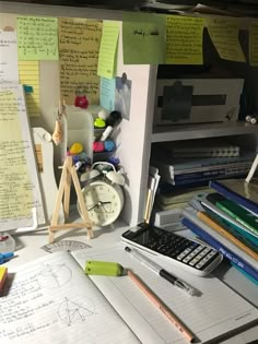 a cluttered desk with papers, pens and a calculator next to it