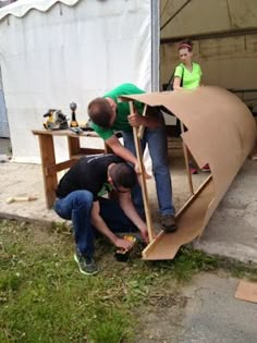 three men are working on a large piece of cardboard