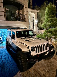 a white jeep is parked in front of a building at night with its lights on