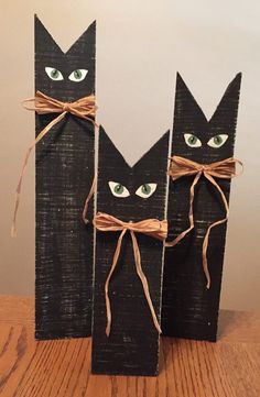 two black cats made out of wood sticks with green eyes and brown ribbon tied around them