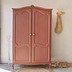 a pink armoire next to a toy truck and giraffe head on the wall