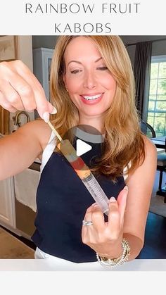 a woman is holding a knife in her hand and pointing to it with the words rainbow fruit kabobs