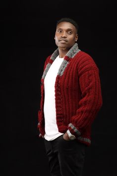 a man wearing a red cardigan standing in front of a black background