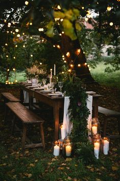 an outdoor dinner table with candles and greenery on the table, surrounded by trees