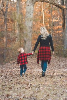 a woman and her child walking through the woods in plaid outfits with trees behind them