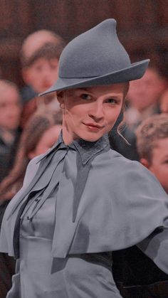 a woman wearing a gray hat and grey dress at a fashion show with people in the background