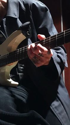 a man is playing an electric guitar with his fingers and fingernails, while sitting in a chair