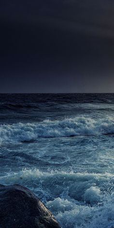 the sun is setting over the ocean with waves crashing in front of it and dark clouds