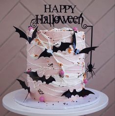 a halloween cake decorated with bats and sprinkles on a white pedestal in front of a brick wall