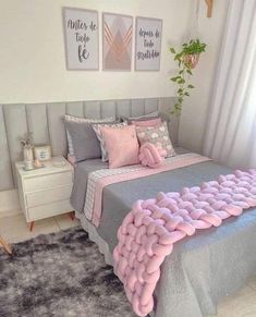 a bed with pink and grey pillows in a bedroom next to two pictures on the wall