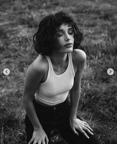 a black and white photo of a woman sitting in the grass with her hands on her knees