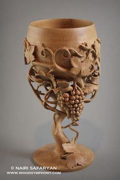 a wooden vase with grapes and vines on it's sides, in the shape of a cup