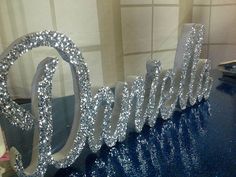 the letters are made out of silver glitters and sit on a blue counter top