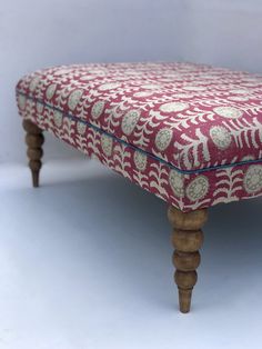 an upholstered footstool with wooden legs and a floral pattern on it