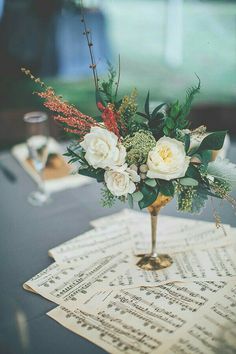 a vase filled with flowers sitting on top of a table next to music sheets and wine glasses