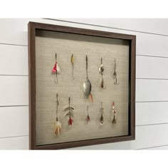 a shadow frame with fishing hooks and spoons hanging from it's sides on the wall