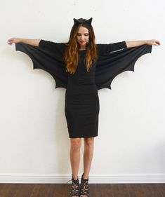 a woman wearing a bat costume standing in front of a wall with her arms outstretched